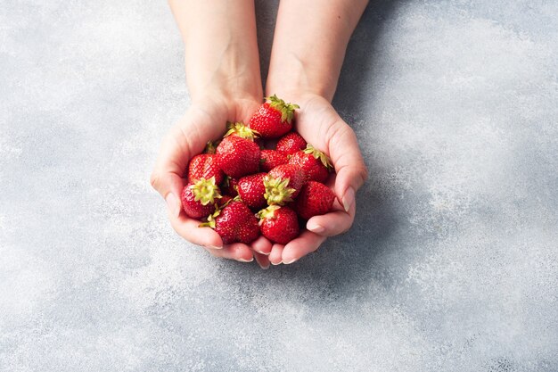 Puñado de jugosas fresas maduras en las manos sobre un fondo de hormigón. Postre dulce y saludable, cosecha de vitaminas. Copie el espacio.