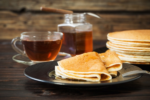 Puncakes con miel y una taza de té en la mesa de madera antigua