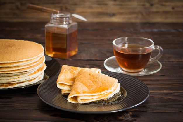 Puncakes mit Honig und Tasse Tee auf alter Holzoberfläche