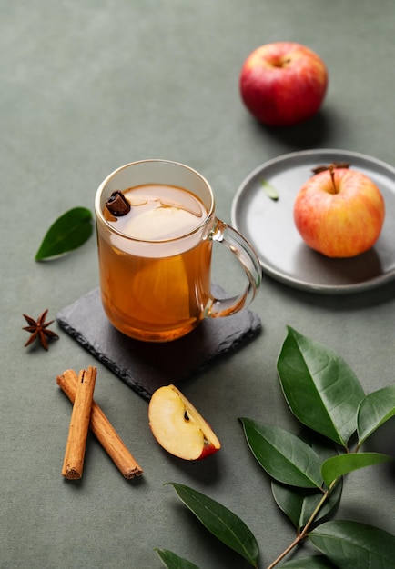 Punch de maçã caseiro com maçãs frescas, canela e especiarias em copo em um fundo verde com frutas frescas e galho Uma bebida quente e saudável de outono