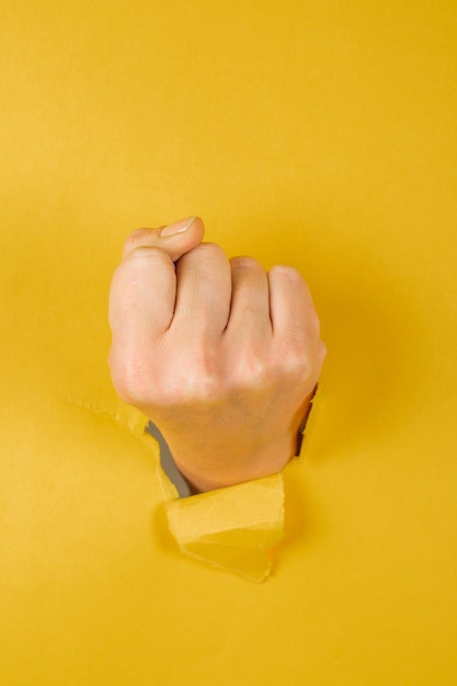 Puño femenino perforando un papel aislado en un fondo amarillo