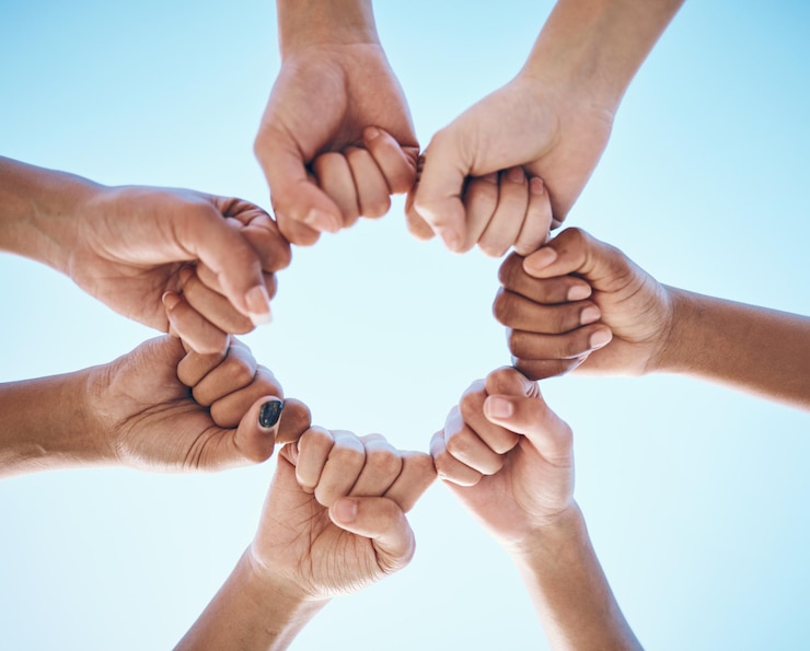 Foto puño de manos y personas en círculo con ángulo bajo para confianza, solidaridad y motivación en el fondo del cielo azul. manos poderosas y amigos, colaboración con la comunidad de esperanza y apoyo a la meta o misión.