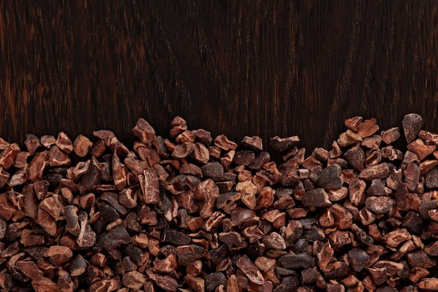 Puntas de cacao sobre tabla de madera marrón Trozos crujientes de granos de cacao pelados, triturados y ligeramente tostados