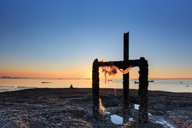 Punto de madera en la playa contra el cielo despejado durante la puesta de sol