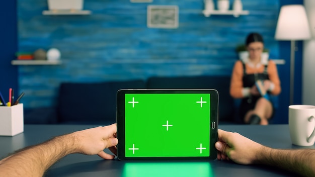Punto de vista de las manos del hombre de negocios sosteniendo la tableta con pantalla verde chroma key display de pie sobre la mesa de escritorio