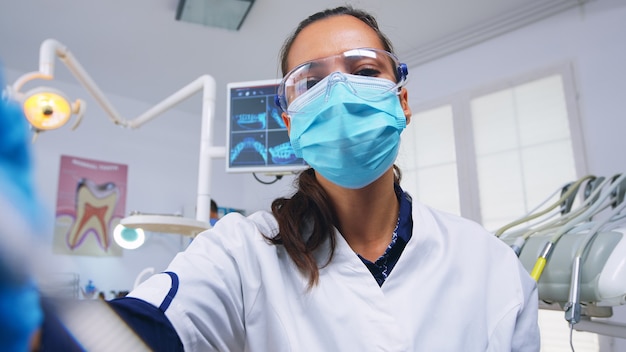 Punto de vista del paciente al estomatólogo que realiza un examen y cuida los dientes con herramientas dentales en una clínica moderna. Médico y enfermera que trabajan en la oficina de ortodoncia moderna con máscara de protección