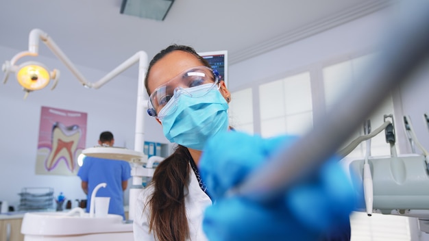 Punto de vista del paciente al médico en el consultorio estomatológico que trata los dientes de la mujer. Especialista en ortodoncia y asistente de hombre que trabaja con máscaras y guantes en la clínica dental moderna.