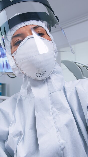 Punto de vista del paciente del dentista con herramientas dentales con traje de protección covid que trata al paciente en la nueva clínica normal. Estomatólogo con equipo de seguridad contra el coronavirus durante el control de atención térmica de la persona.