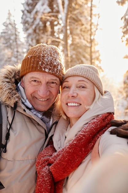 Punto de vista vertical de la feliz pareja de ancianos tomando una foto selfie mientras disfruta de una caminata en el bosque de invierno