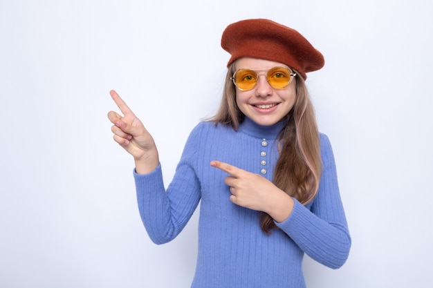 Puntos sonrientes al lado hermosa niña con gafas con sombrero aislado en la pared blanca con espacio de copia