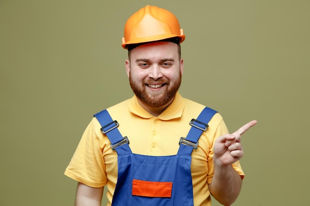 Puntos sonrientes al lado joven constructor hombre en uniforme aislado sobre fondo verde