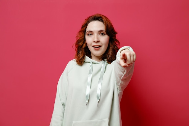 Puntos sonrientes a la cámara joven hermosa chica en suéter blanco aislado sobre fondo rosa