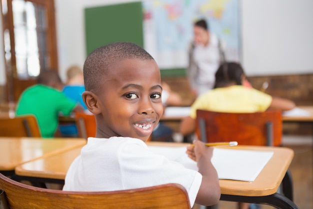 Pupila fofa sorrindo para a câmera em sua mesa na sala de aula