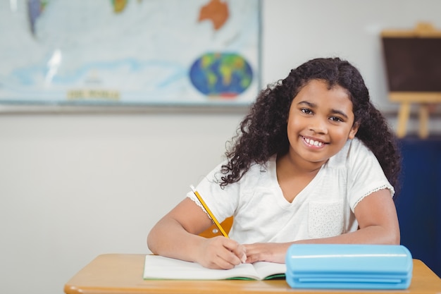 Pupila sorridente que trabalha em sua mesa em uma sala de aula