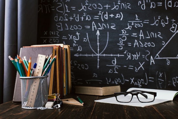 Pupitre en el aula, con libros sobre fondo de pizarra con fórmulas escritas