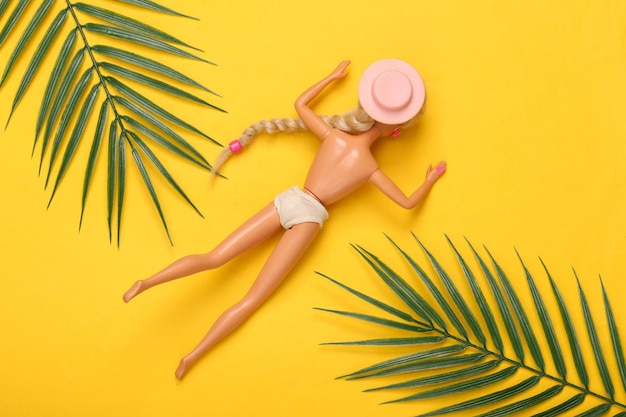 Foto puppe in einem badeanzug sonnt sich auf gelbem hintergrund mit palmblättern sommerurlaub strand sonnenbaden