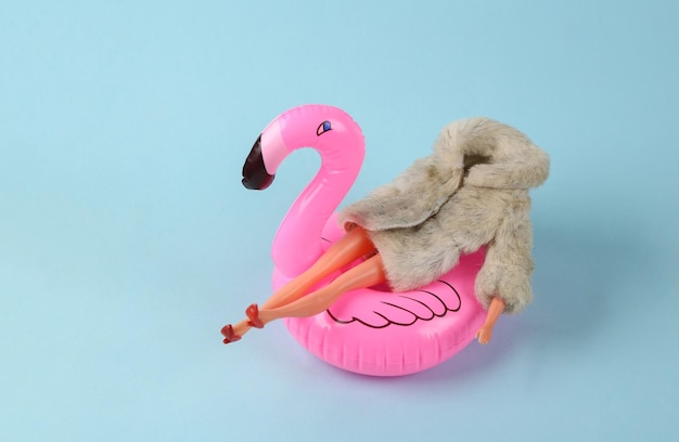 Puppe Mannequin in warmem Pelzmantel in aufblasbarem Flamingo auf rosa hellem Hintergrund globale Erwärmung Minimalismus erschossen Konzeptkunst