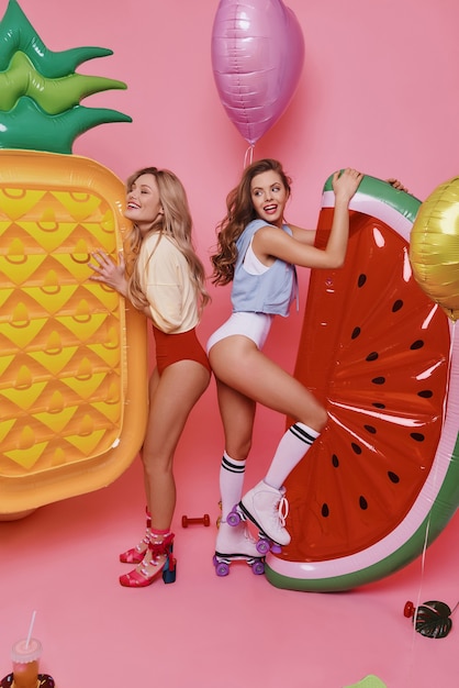 pura felicidad. Longitud total de dos atractivas mujeres jóvenes en traje de baño jugando con adornos de frutas