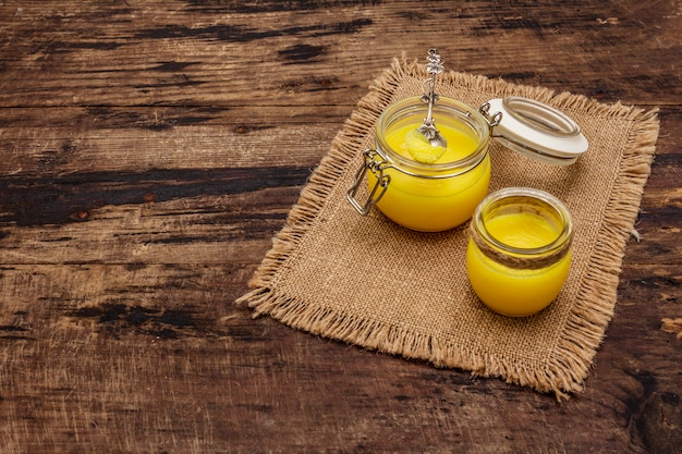 Pura o desi ghee (ghi), mantequilla derretida clarificada. Concepto de dieta a prueba de balas de grasas saludables o plan de estilo paleo. Tarro de cristal, cuchara de plata sobre tela de saco vintage.