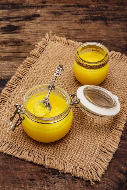 Pura o desi ghee (ghi), mantequilla derretida clarificada. Concepto de dieta a prueba de balas de grasas saludables o plan de estilo paleo. Tarro de cristal, cuchara de plata sobre tela de saco vintage.