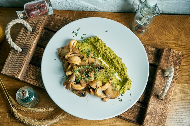 Puré de brócoli con champiñones fritos en un plato blanco sobre una plancha de madera. Comida vegetariana. Vista superior, endecha plana