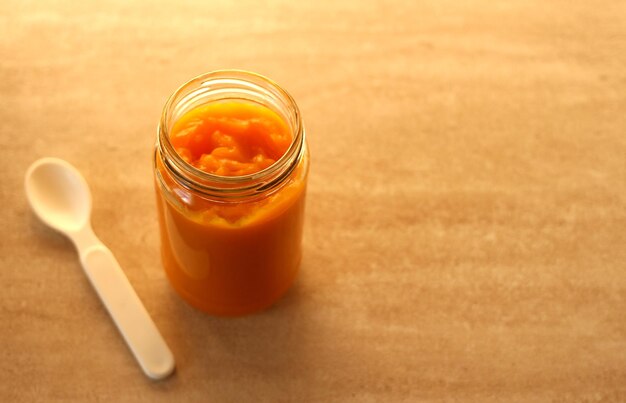 Puré de calabaza baby en un frasco de vidrio con una cuchara blanca