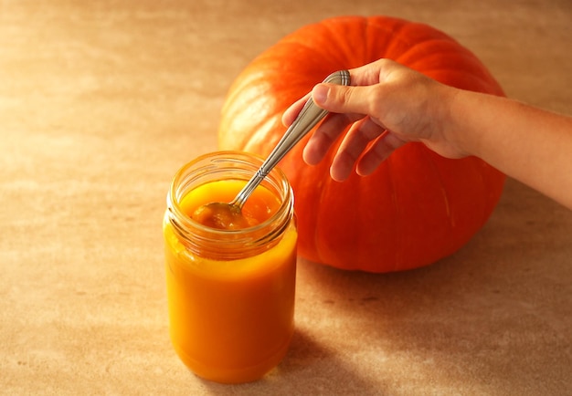 Puré de calabaza fresca en un frasco con manos de niños y calabaza entera fresca sobre un fondo beige