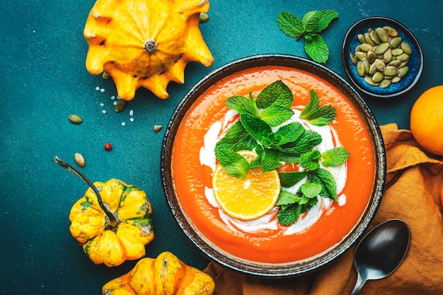 Purê de sopa de abóbora doce com creme de laranja e hortelã Inverno ou outono comida vegetariana saudável comida lenta Tigela de sopa sobre fundo de mesa azul verde Vista superior