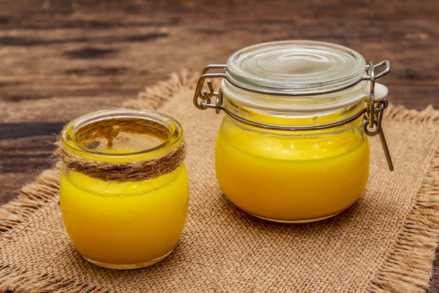 Pure oder Desi Ghee (Ghi), geklärte geschmolzene Butter. Kugelsicheres Diätkonzept der gesunden Fette oder Paläoartplan. Glas, silberner Löffel auf Weinlesesackleinen.