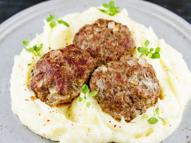 Puré de papas y albóndigas en un plato gris, decorado con albahaca fresca