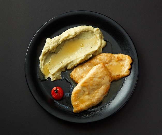 Puré de papas con filetes de pollo en un plato negro aislado en un fondo negro