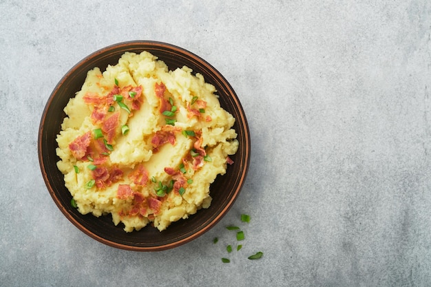 Puré de papas hervidas Puré de papas con tocino con pimiento de cebolla verde y queso cheddar en un tazón sobre fondos de madera clara Delicioso puré de papas cremoso Vista superior