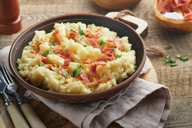 Puré de papas Puré de papas con tocino con pimiento de cebolla verde y queso cheddar en un tazón sobre fondos de madera antiguos Delicioso puré de papas cremoso Vista superior