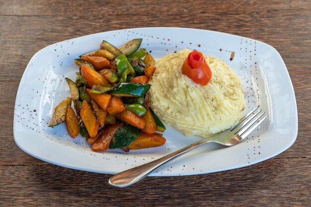 Puré de papas con vegetales fritos en un plato blanco