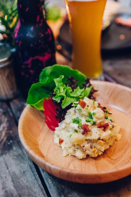 Puré de patata con tocino servido con ensalada en plato de madera.