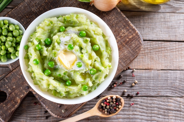 Puré de patatas con guisantes y especias en un cuenco de cerámica sobre una mesa de madera con espacio libre. Comida vegetariana saludable