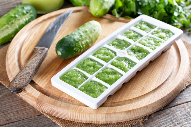 Puré de pepino congelado en bandejas de cubitos de hielo listo para congelar sobre una tabla de cortar sobre una mesa de madera. Concepto de comida congelada.