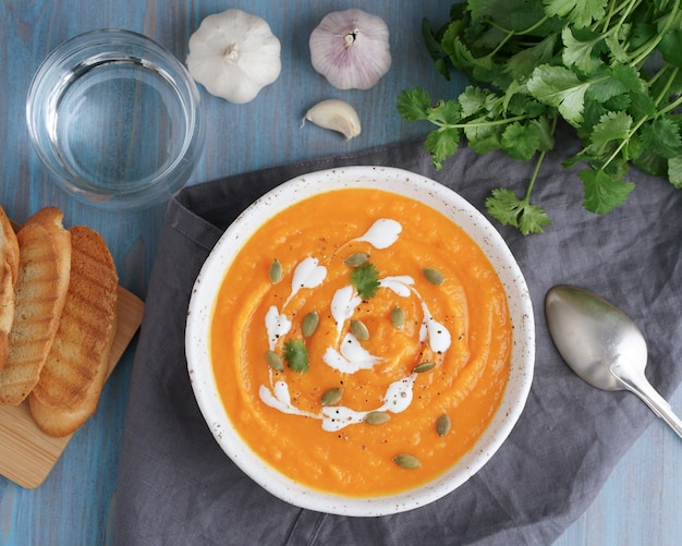 Puré poner crema de la sopa de Pupmkin, almuerzo vegetariano dietético en la tabla de madera azul, visión superior. Vaso de agua