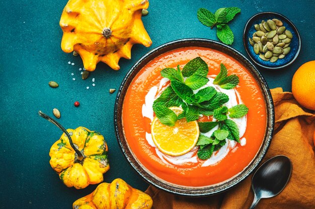 Puré de sopa de calabaza dulce con crema de naranja y menta Invierno u otoño vegetariano saludable comodidad comida lenta Tazón de sopa sobre fondo de mesa azul verde Vista superior