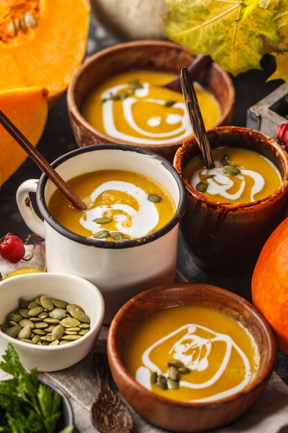 Puré de la sopa de la calabaza de otoño con crema en tazas, el paisaje del otoño. Concepto de comida vegana saludable.