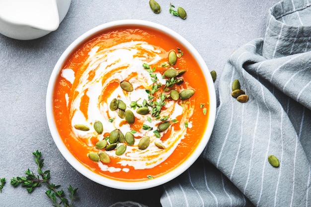 Puré de sopa cremosa de calabaza con crema de semillas de calabaza y tomillo Comida lenta vegetariana saludable de invierno u otoño Cuenco de sopa blanco sobre fondo de mesa gris Vista superior