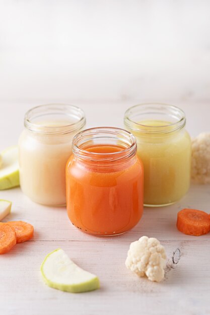 Puré de verduras para bebés de zanahorias, calabacines, coliflor en frascos de vidrio en blanco