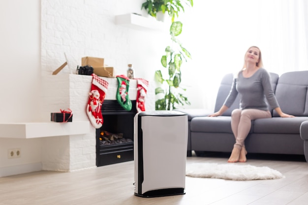 Purificador de aire en una sala de estar, mujer que trabaja con un portátil con filtro para sala limpia