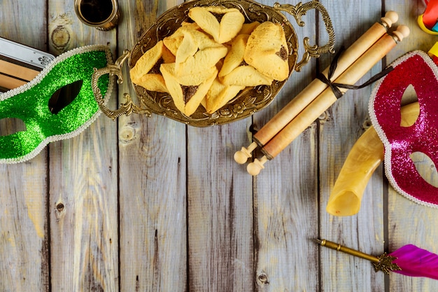 Purim tradicional con galletas hamantaschen, matraz y máscara de carnaval sobre fondo de madera