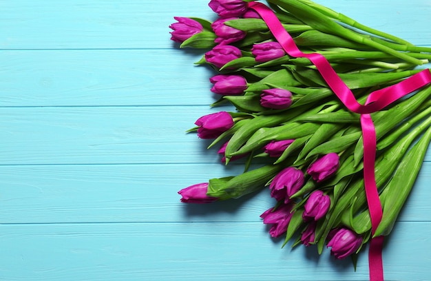 Púrpura hermosos tulipanes con cinta sobre fondo de madera azul