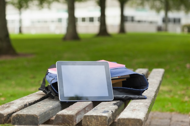 Purpurrote Schultasche und Tablette, die auf Parkbank liegen