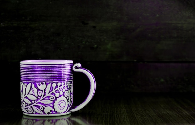 Purpurrote Tasse auf altem hölzernem dunklem Hintergrund