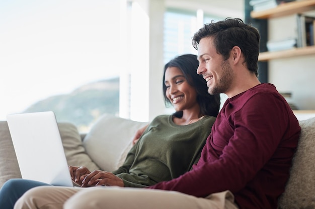 Pusieron el nosotros en el fin de semana Foto de una joven pareja cariñosa usando su computadora portátil mientras se sienta en el sofá en casa