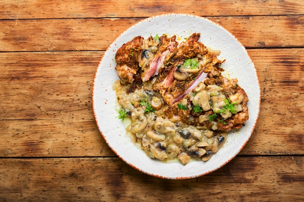 Putenfleisch in Käsepanade mit Pilzsauce. Putenschnitzel auf rustikalem Holztisch