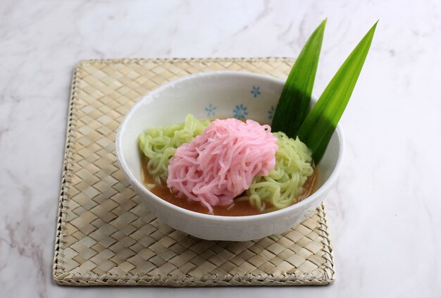 Putu Mayang o Petulo, refrigerio tradicional javanés de Indonesia hecho de hebras de harina de arroz enrolladas en una bola con colorante alimentario, servido con leche de coco y jarabe de azúcar de palma. Fondo blanco